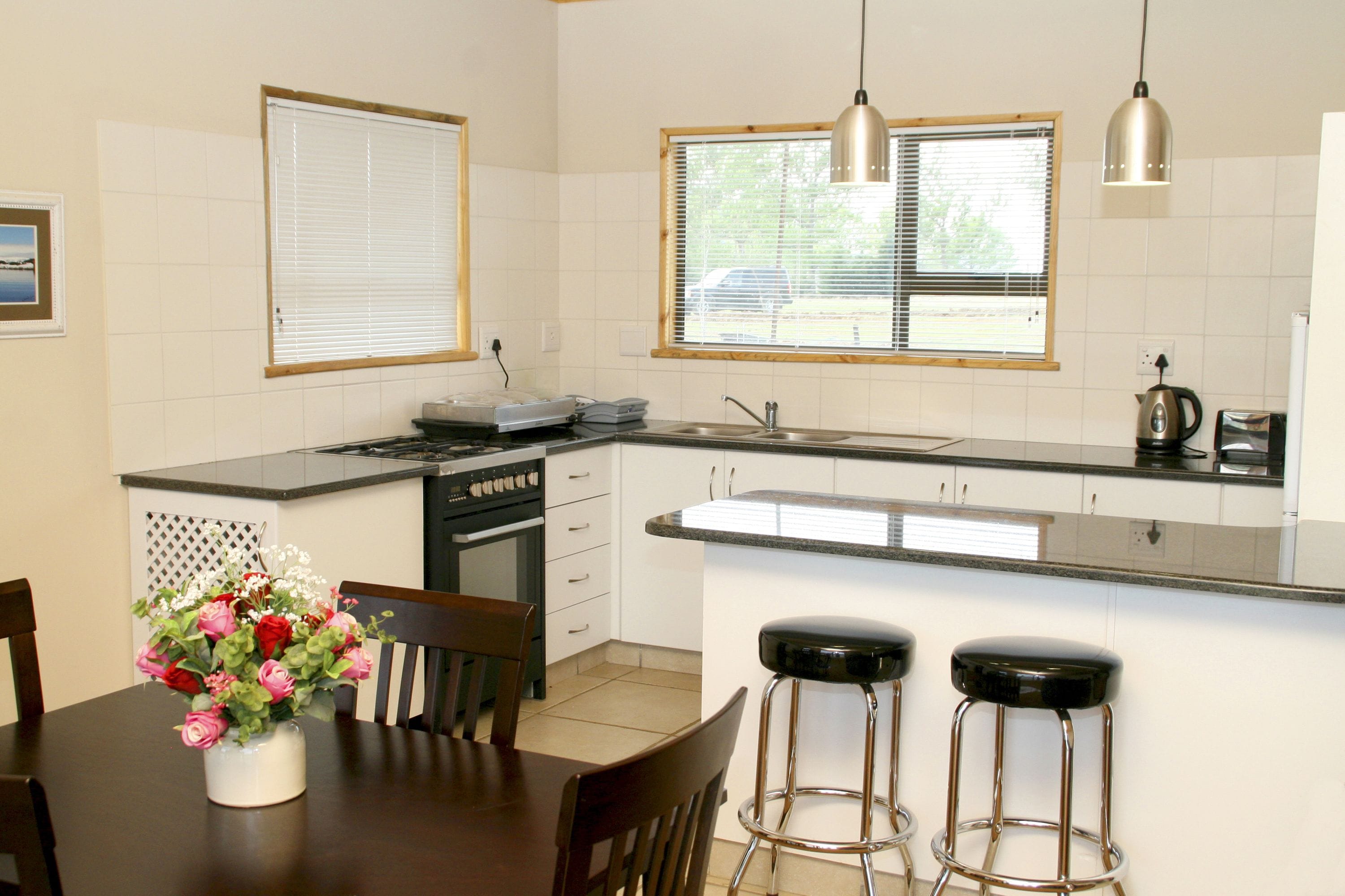 A kitchen with a dining area, a stove, a sink, and two bar stools.