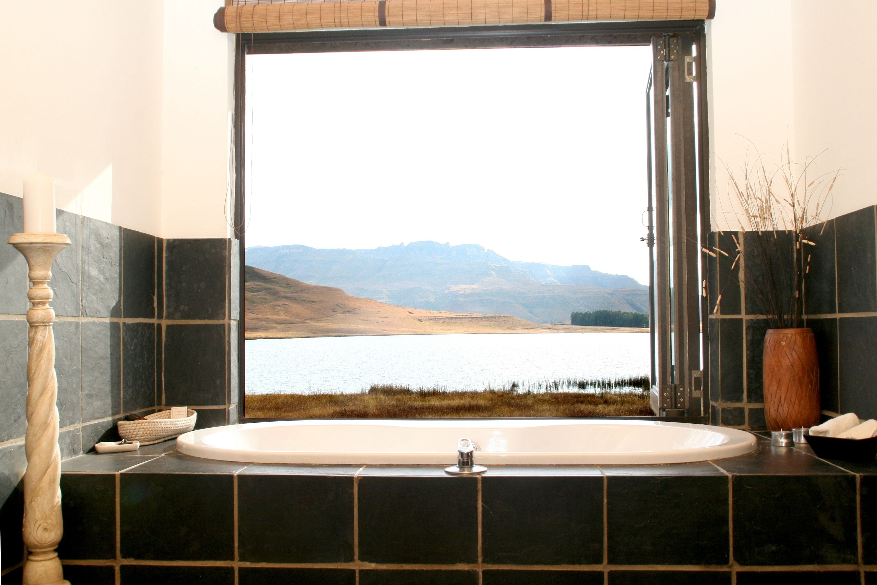 Un baño con una bañera grande, vista a un lago y montañas al fondo.
