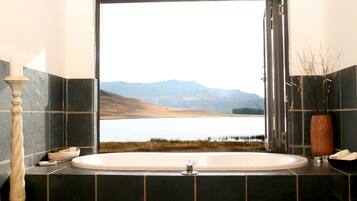 Un baño con una bañera grande, vista a un lago y montañas al fondo.