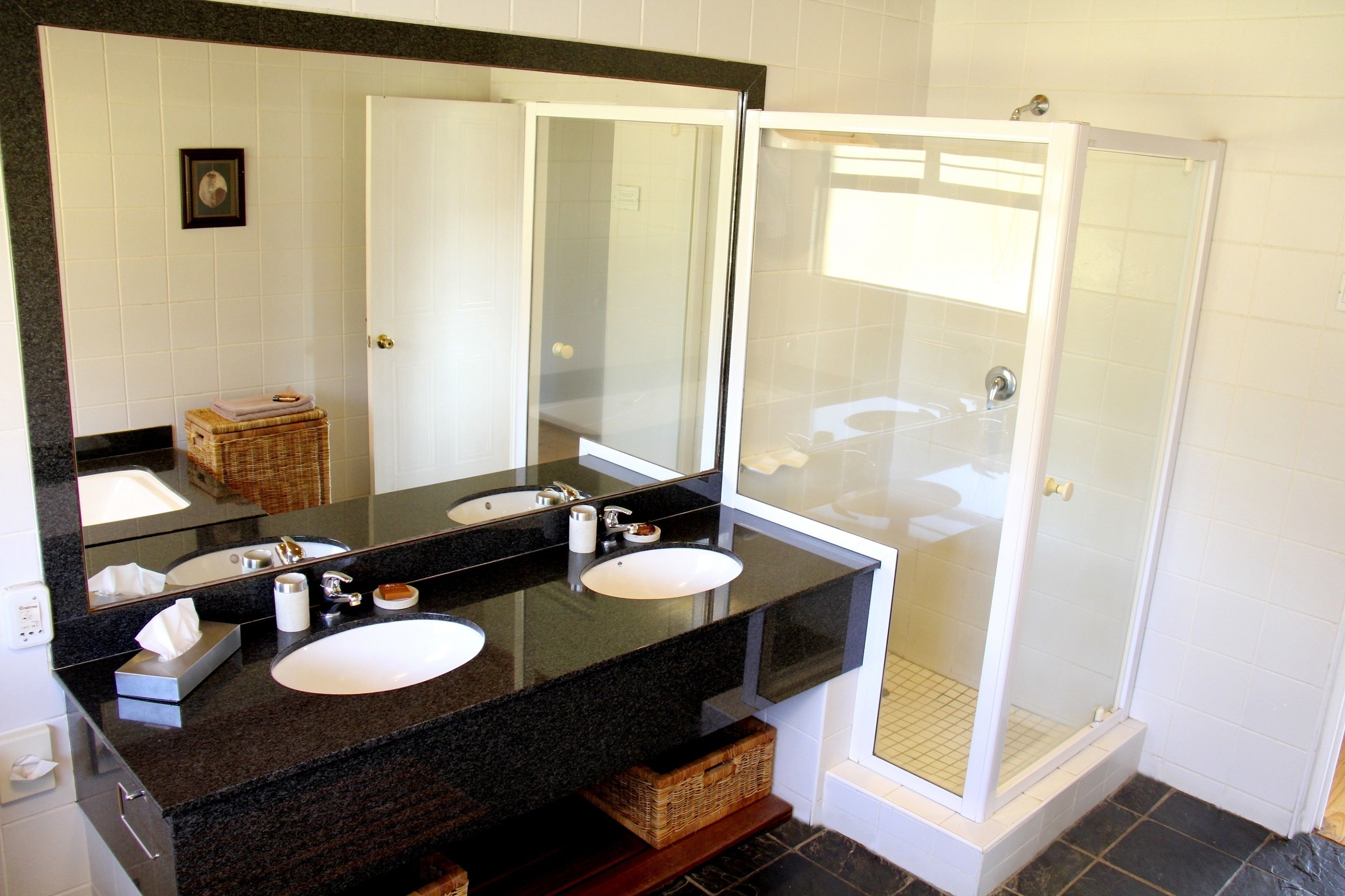 A bathroom with two sinks, a large mirror, and a glass-enclosed shower.