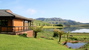Uma cabana de madeira com varanda com vista para um lago e montanhas.