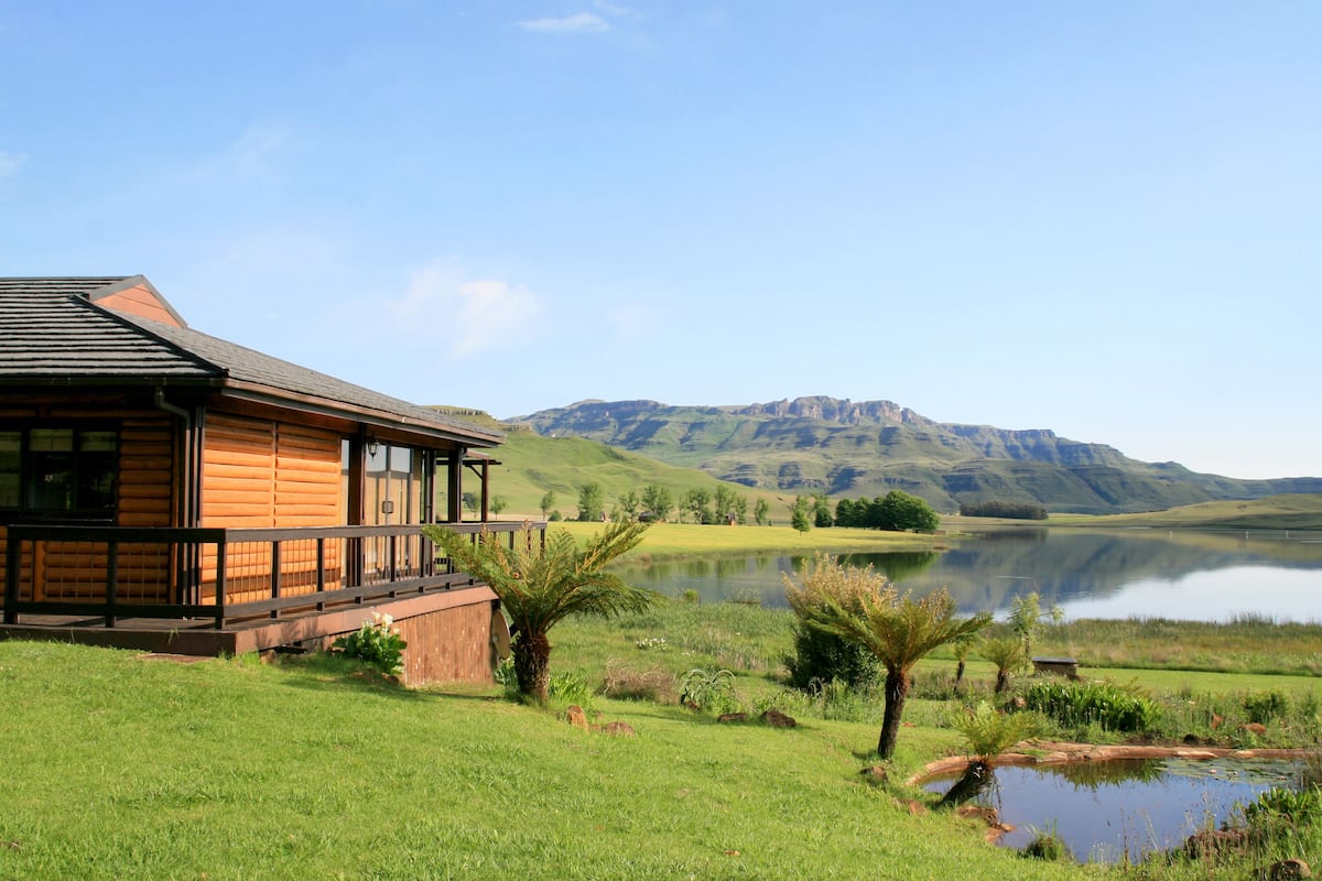 A wooden cabin with a balcony overlooking a lake and mountains.