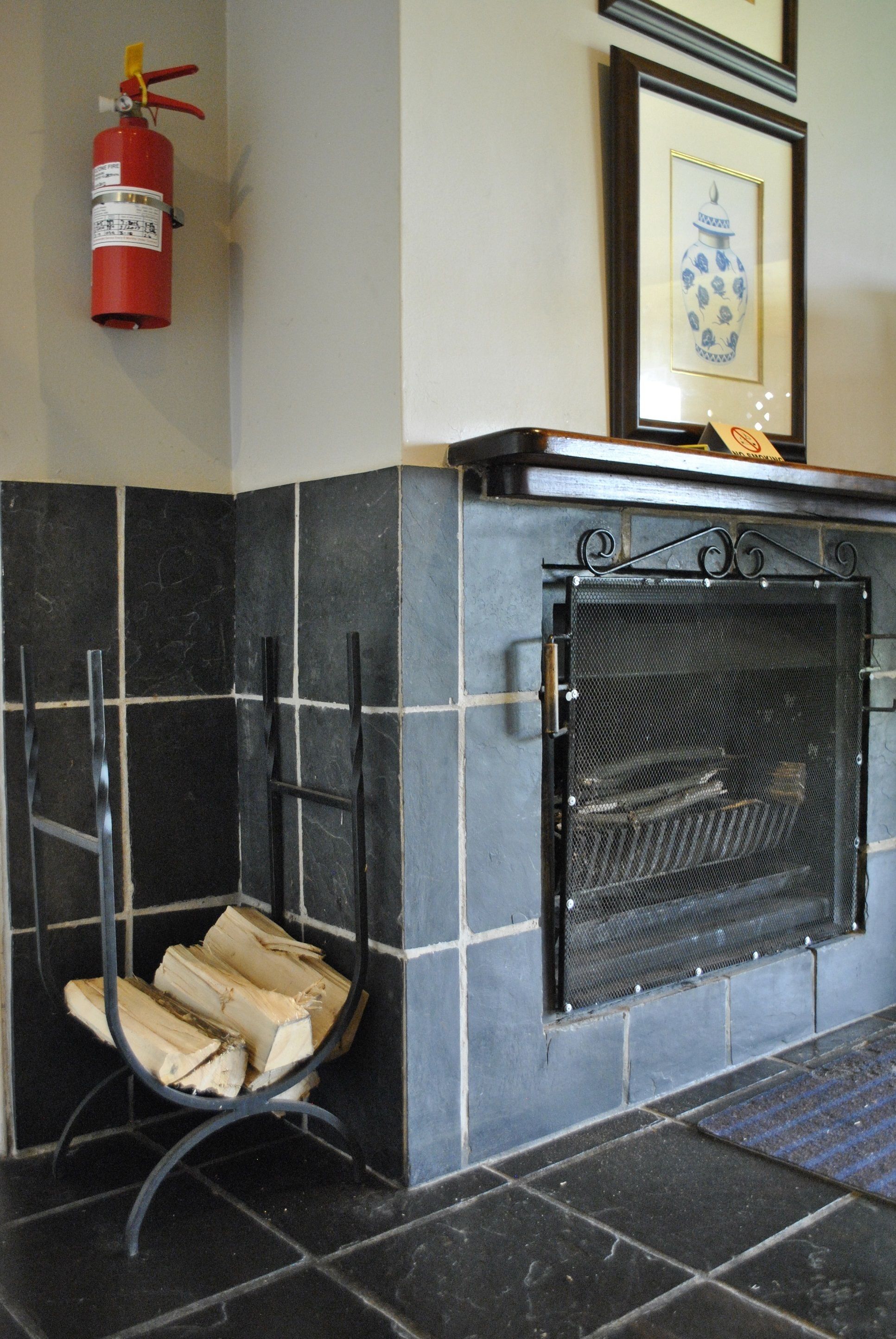 A fireplace with a metal screen, a fire extinguisher on the wall, and a framed picture above it.