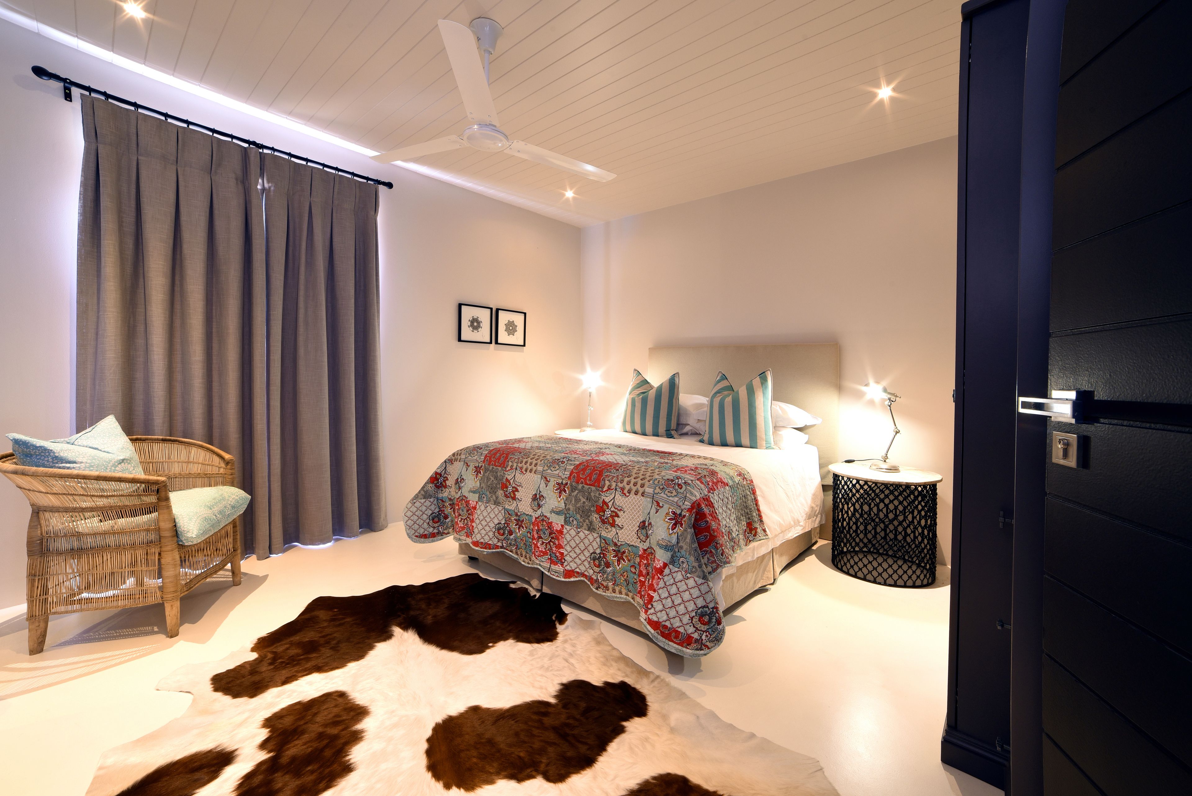 A bedroom with a bed, a chair, a small round table, and a cowhide rug.