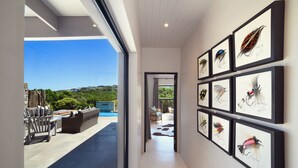 Un pasillo con señuelos de pesca enmarcados en la pared, que conduce a un patio con mobiliario exterior.