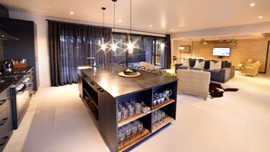 Una cocina moderna con una isla central, electrodomésticos integrados y un área de comedor con sofá y televisor.