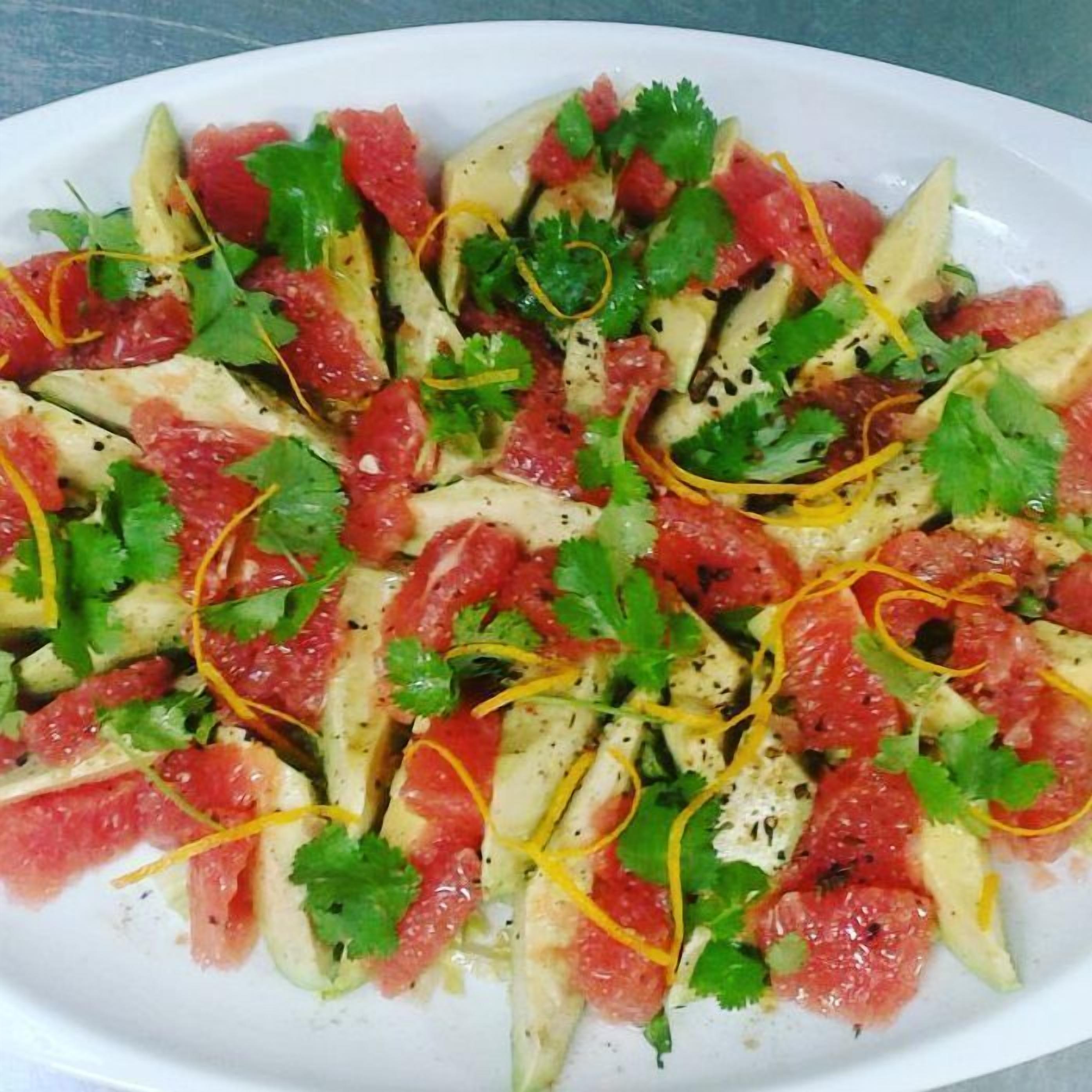 A white oval plate with a salad consisting of thinly sliced cucumbers, red tomatoes, and green herbs, possibly cilantro, with a drizzle of dressing.