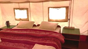 Ein Einzelbett mit rot-weiß gemustertem Bettbezug, zwei Nachttische und zwei mit Vorhängen versehene Fenster.