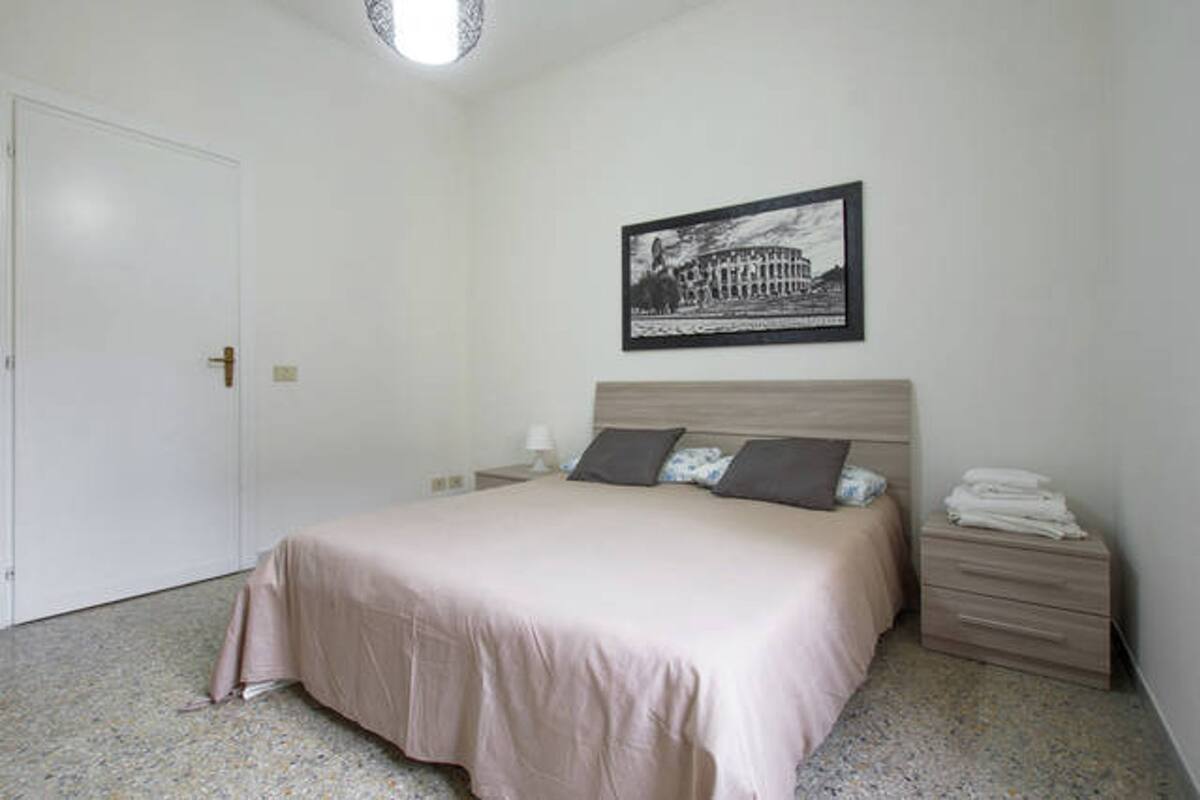 A bedroom with a bed, a nightstand, a framed picture on the wall, and a door.