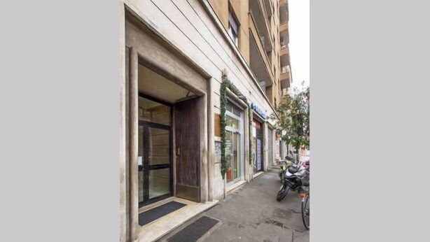 A narrow street with buildings on either side. There are storefronts with visible signage and a motorcycle parked on the right. - Affittacamere Il Porto (Rome)