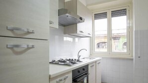 A compact kitchen with white cabinets, a gas stove, a sink, and a window with a view of the outside. - Affittacamere Il Porto (Rome)