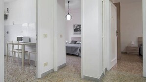 A hotel room with a bed, bedside table, and a small desk with a chair. There is a door leading to another room. - Affittacamere Il Porto (Rome)