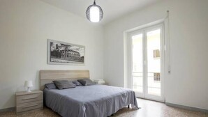 A bedroom with a bed, a nightstand, a lamp, a framed picture on the wall, and a large window. - Affittacamere Il Porto (Rome)