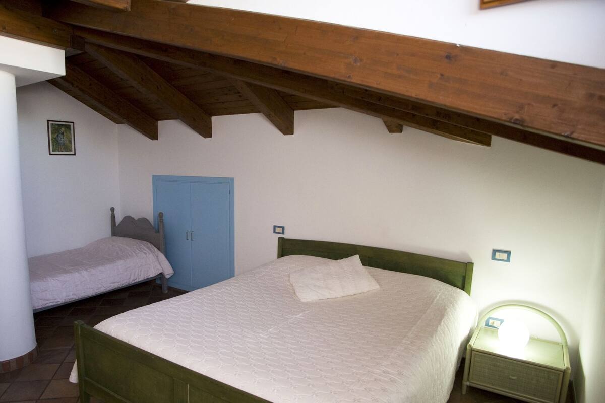 A bedroom with a wooden bed, a blue wardrobe, and a bedside table with a lamp.