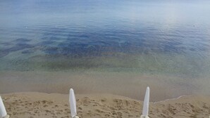 A beach with clear water, a sandy shore, and two white umbrellas. - All'ombra del palmeto (Taranto)