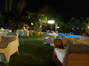 An outdoor pool area with lounge chairs and tables, surrounded by palm trees and string lights. - All'ombra del palmeto (Taranto)