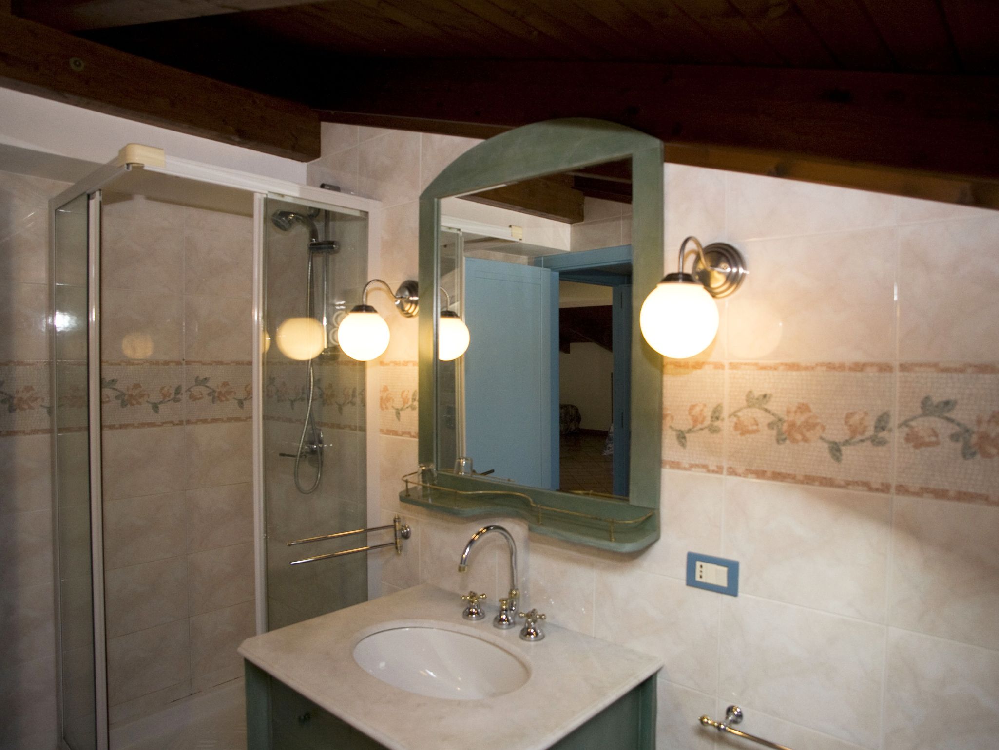 A bathroom with a glass shower door, a sink with a mirror above it, and wall-mounted lights.