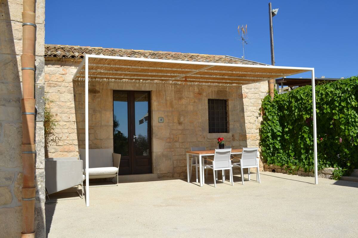 A stone building with a covered patio, a table with chairs, and a small window.