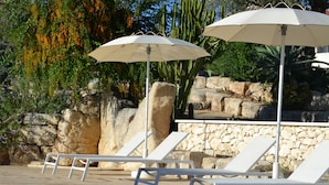 A pool area with white lounge chairs and umbrellas, surrounded by rocks and cacti. - Antica Masseria Timparuci (Modica)