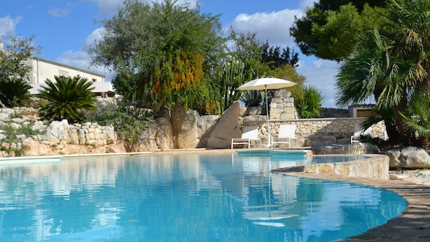 A swimming pool with a stone wall, lounge chairs, and a pergola. - Antica Masseria Timparuci (Modica)