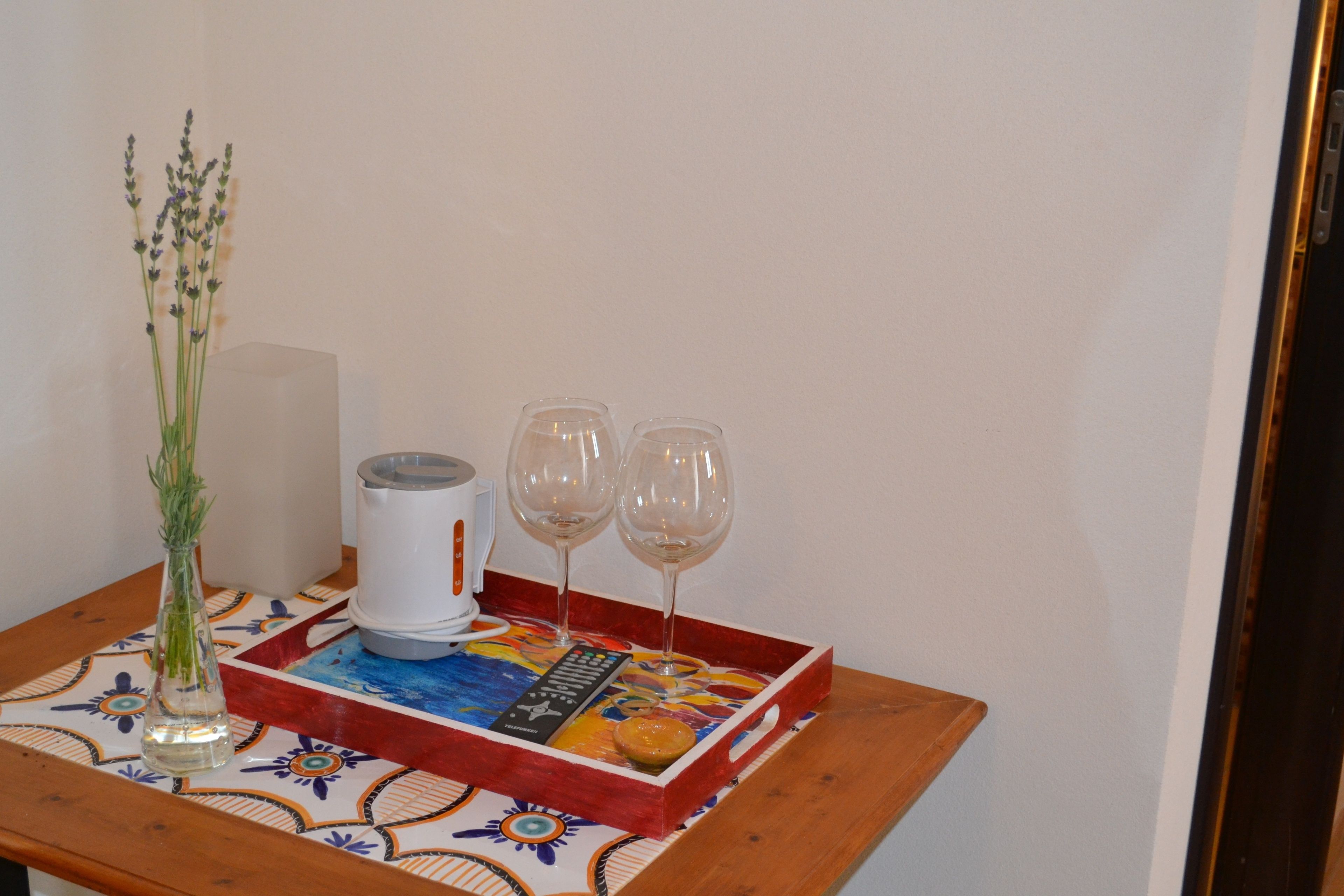 A tray with a remote control, two wine glasses, and a vase with a plant on a table with a colorful tablecloth.