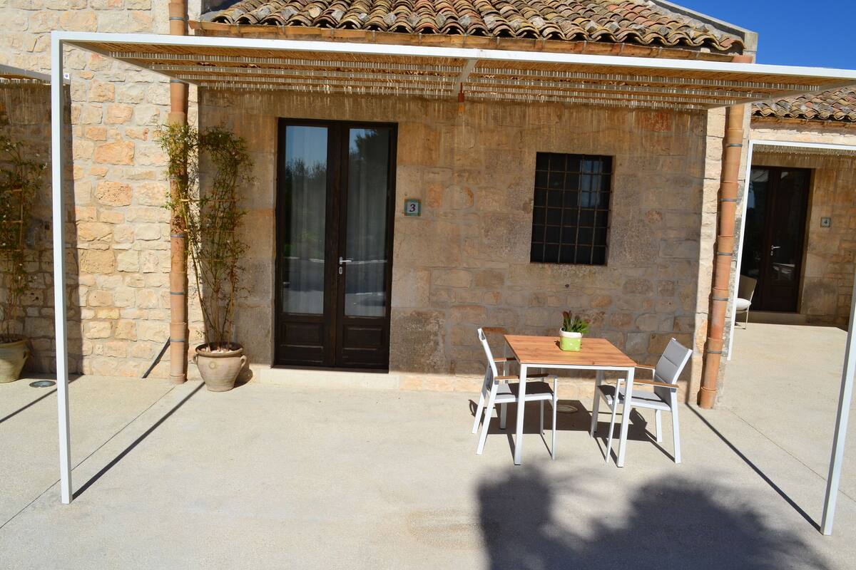 A stone building with a tiled roof, a wooden table with chairs, and a potted plant.