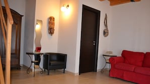 A room with a red sofa, a black armchair, a small table, and a door. - Antica Masseria Timparuci (Modica)