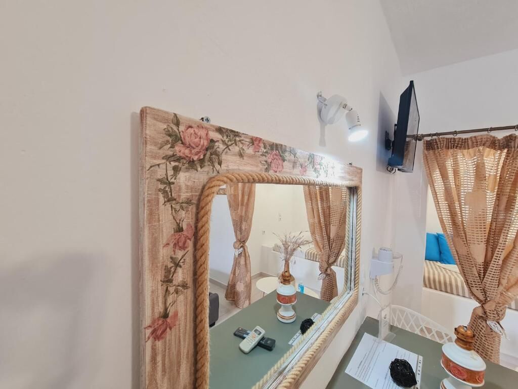 A room with a large mirror, a small table with a vase, a remote control, and a piece of paper.