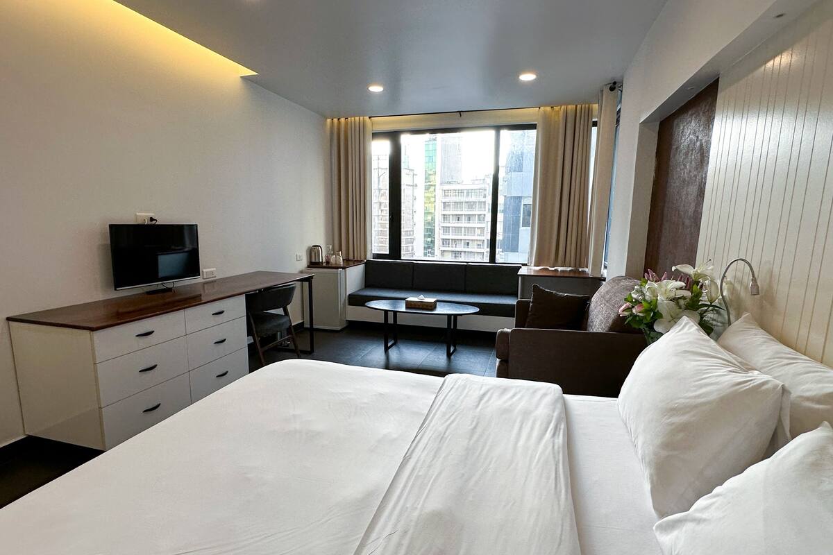 A hotel room with a bed, a desk, a TV, a window with curtains, and a sofa.