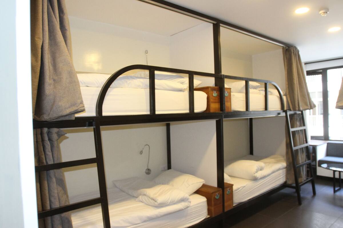 A bunk bed room with a wooden ladder, a small table, and a window with curtains.