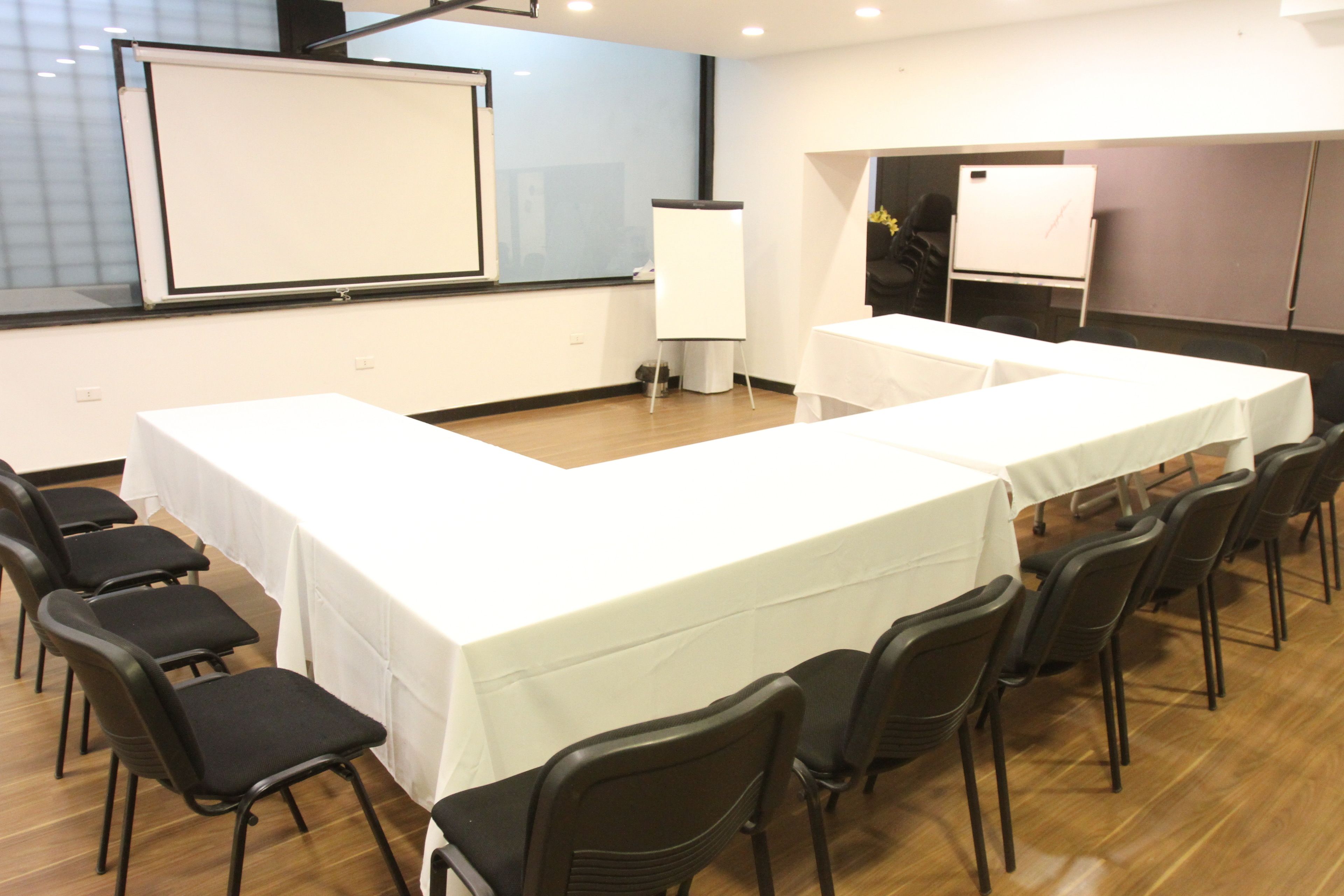 Uma sala de conferência com uma mesa comprida, cadeiras, um quadro branco e uma tela de projetor.