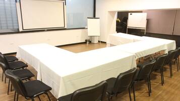 Uma sala de conferência com uma mesa comprida, cadeiras, um quadro branco e uma tela de projetor.