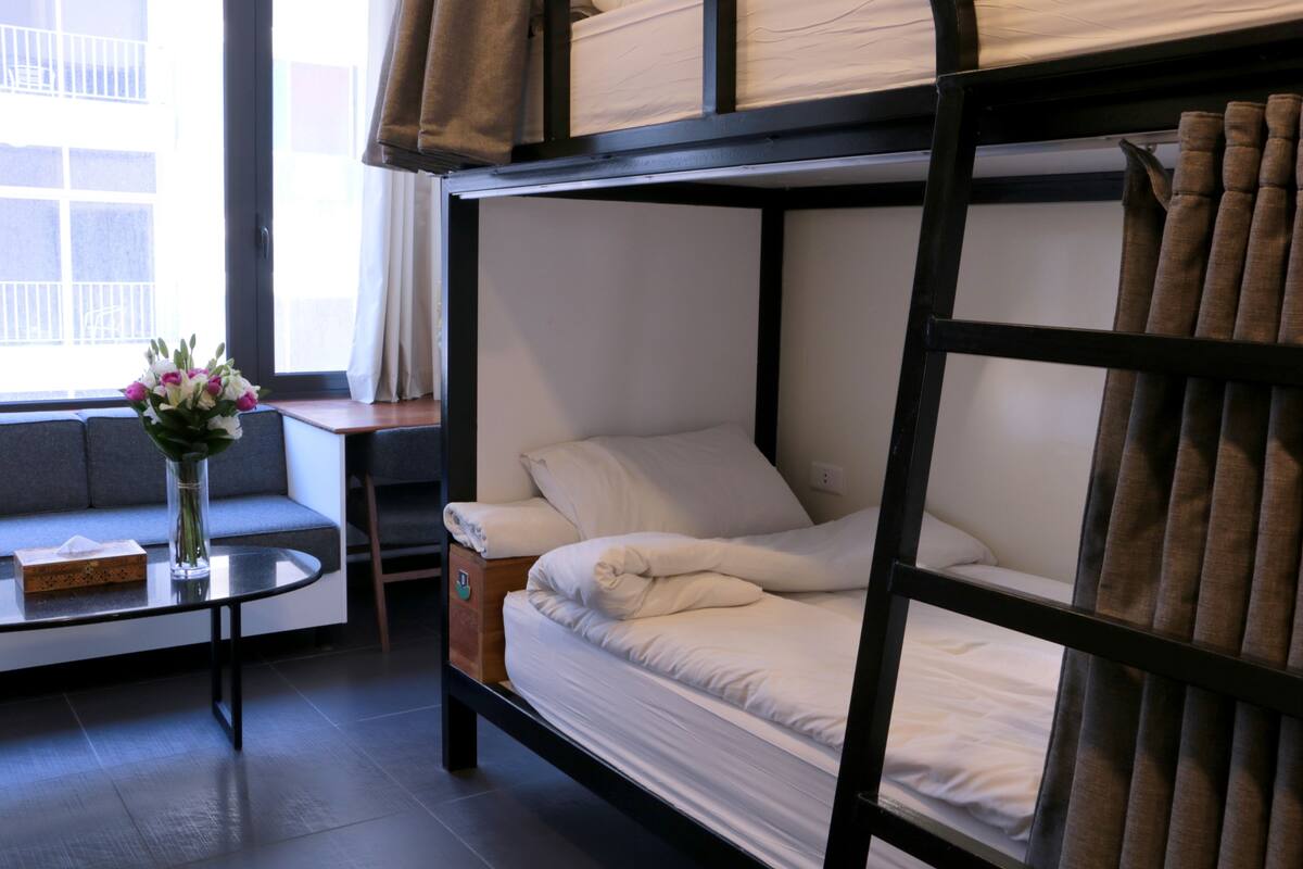 A bunk bed with white bedding, a vase with flowers, and a table with a box and tissue.