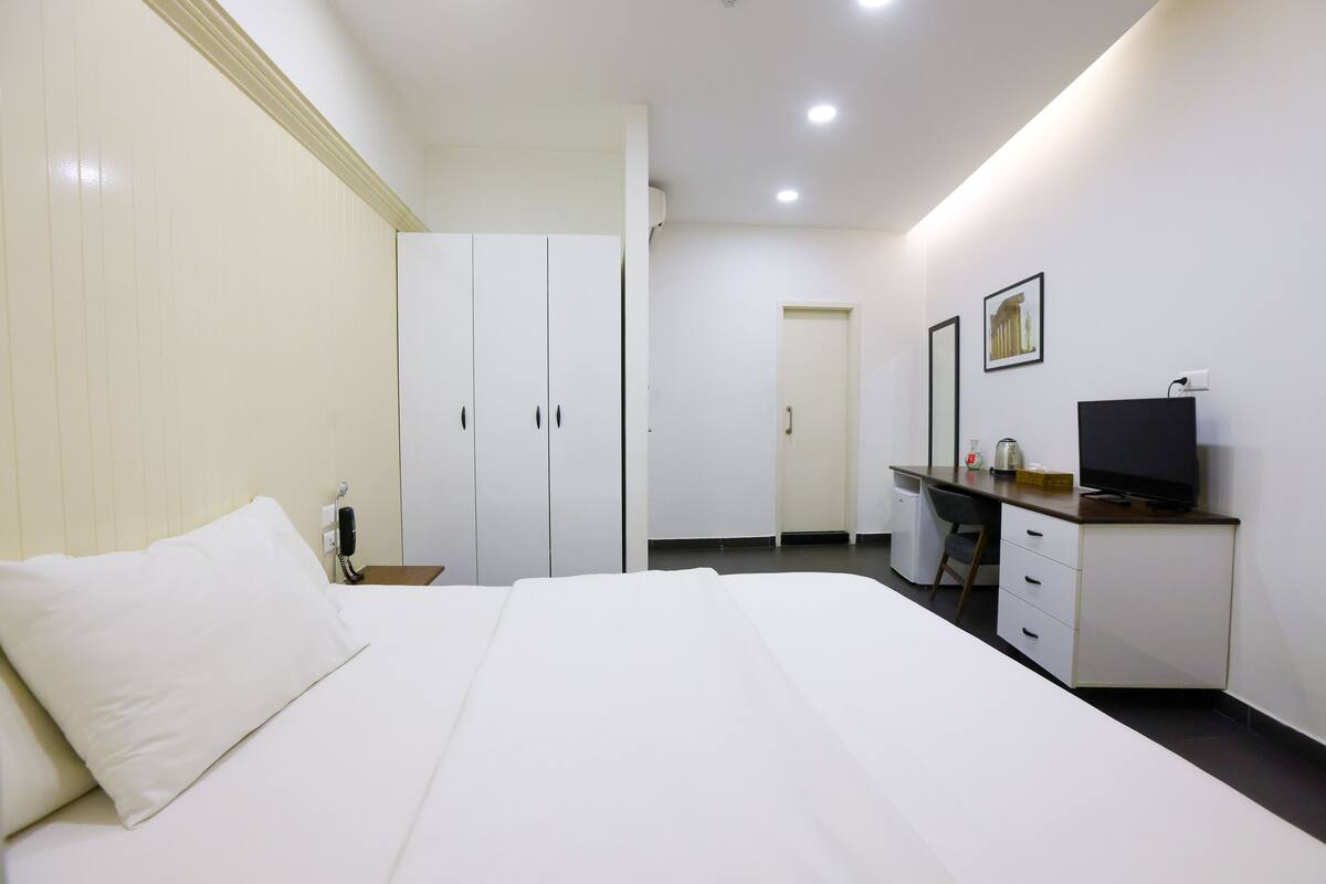 A hotel room with a bed, a desk with a computer, a chair, and a television.