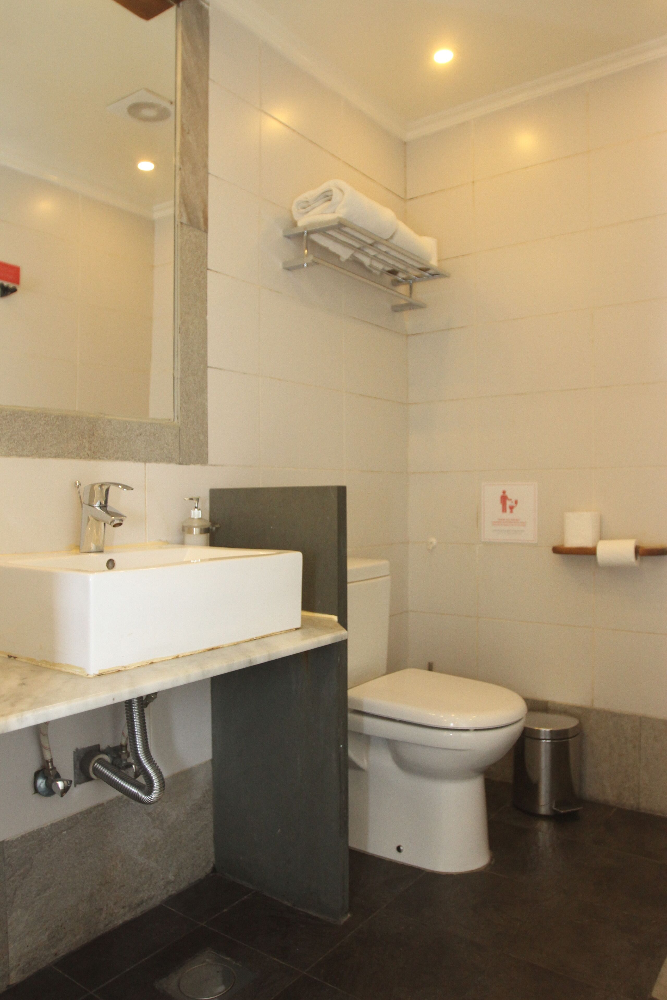 A modern bathroom with a white sink, a toilet, a trash can, and a towel rack.