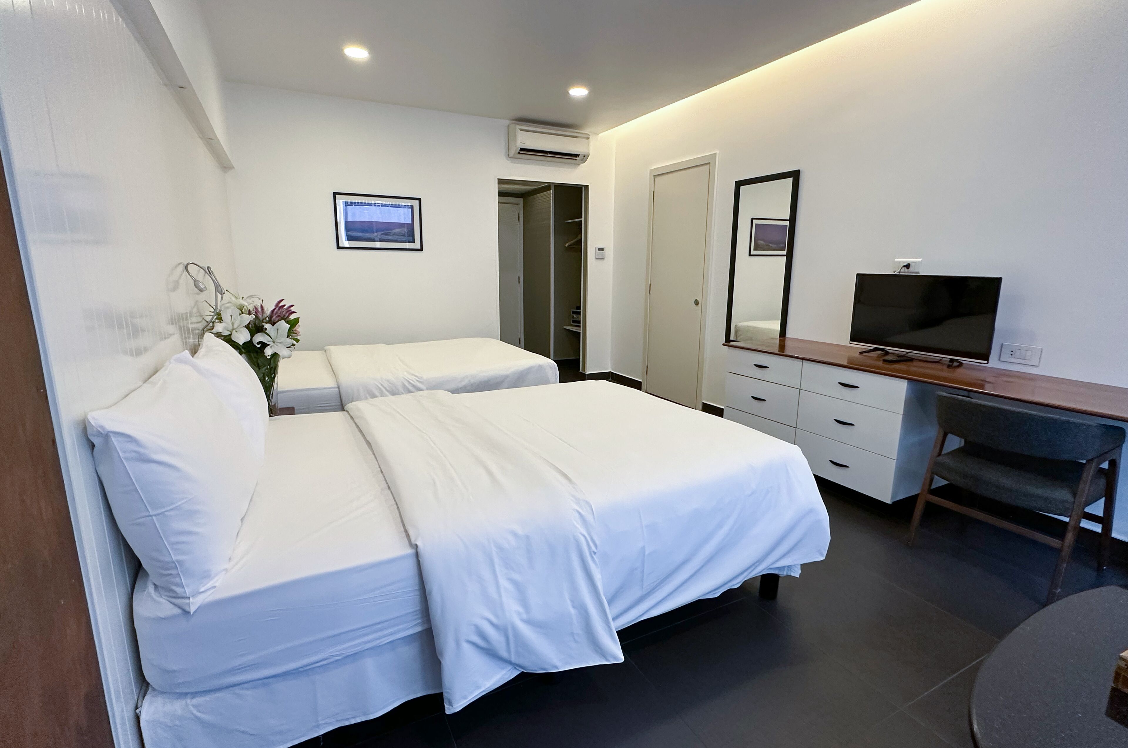 A hotel room with two beds, a desk, a TV, and a mirror.