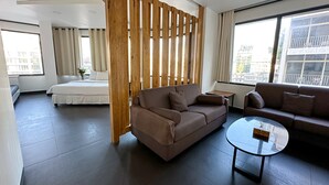 A modern hotel room with a large bed, two sofas, a glass coffee table, and a wooden partition. - Hamra Urban Gardens (Beirut)