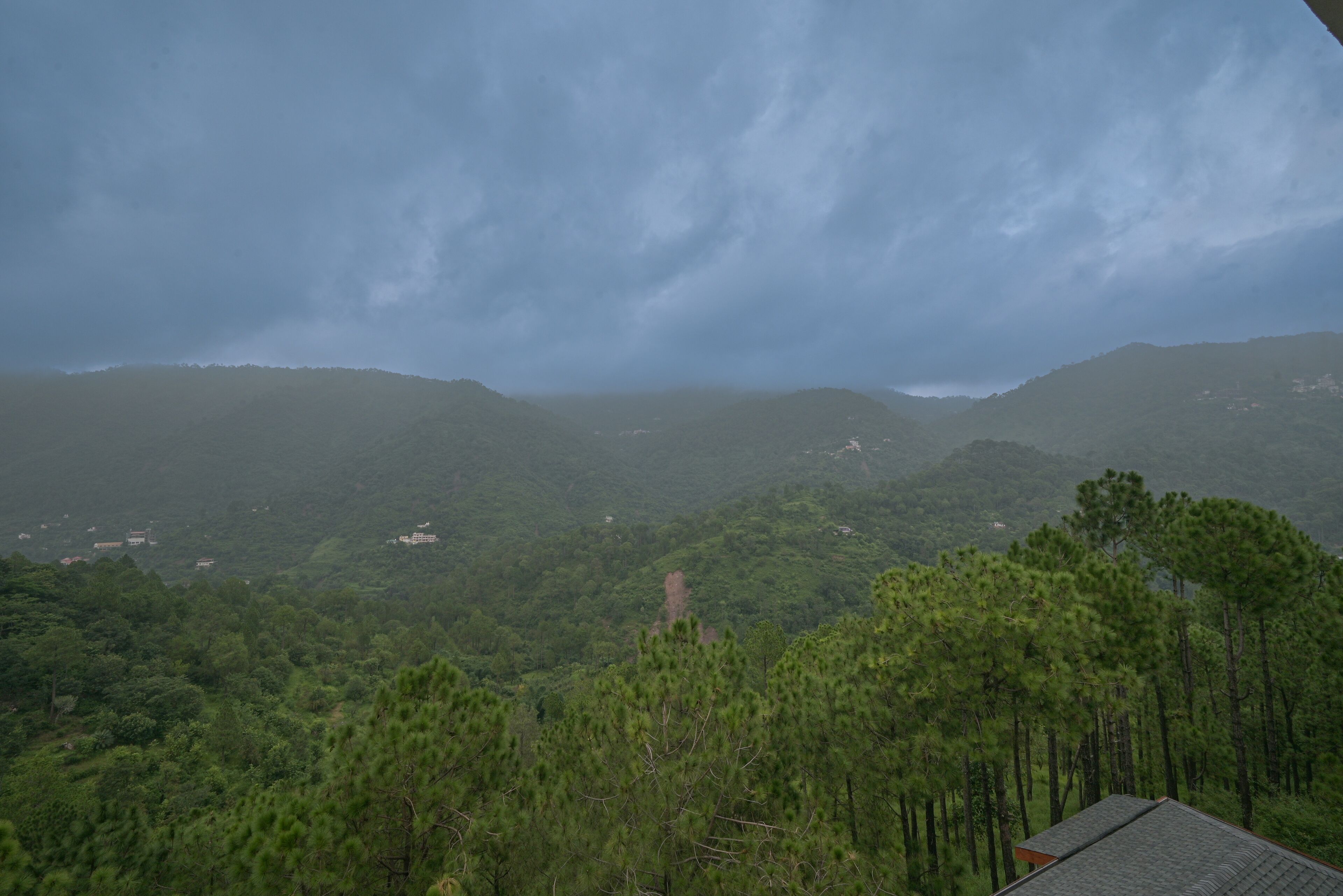A mountainous landscape with dense forest and a small building with a sloped roof.