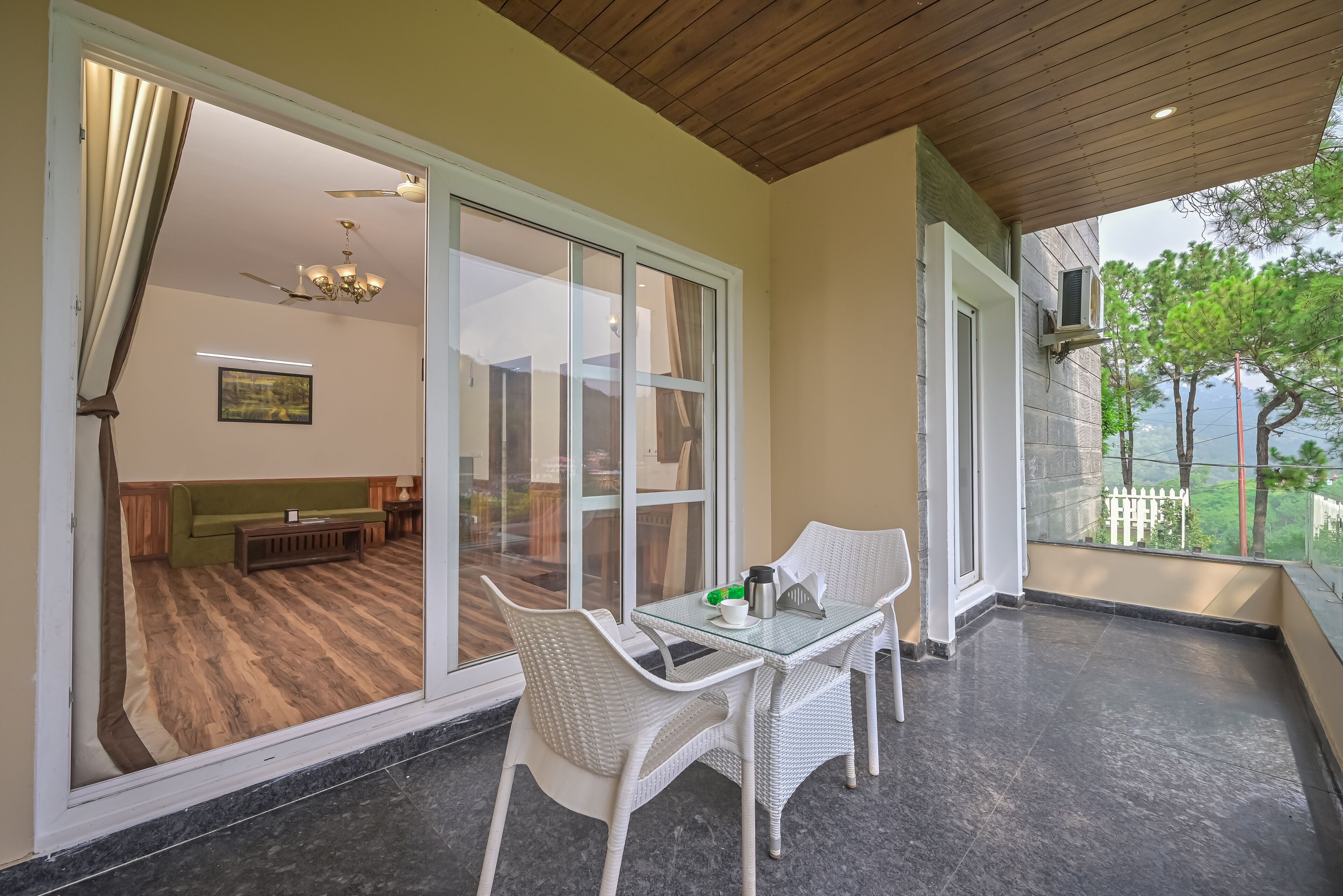 Un balcon avec une table et des chaises en verre, une vue sur l’intérieur et un plafond en bois.