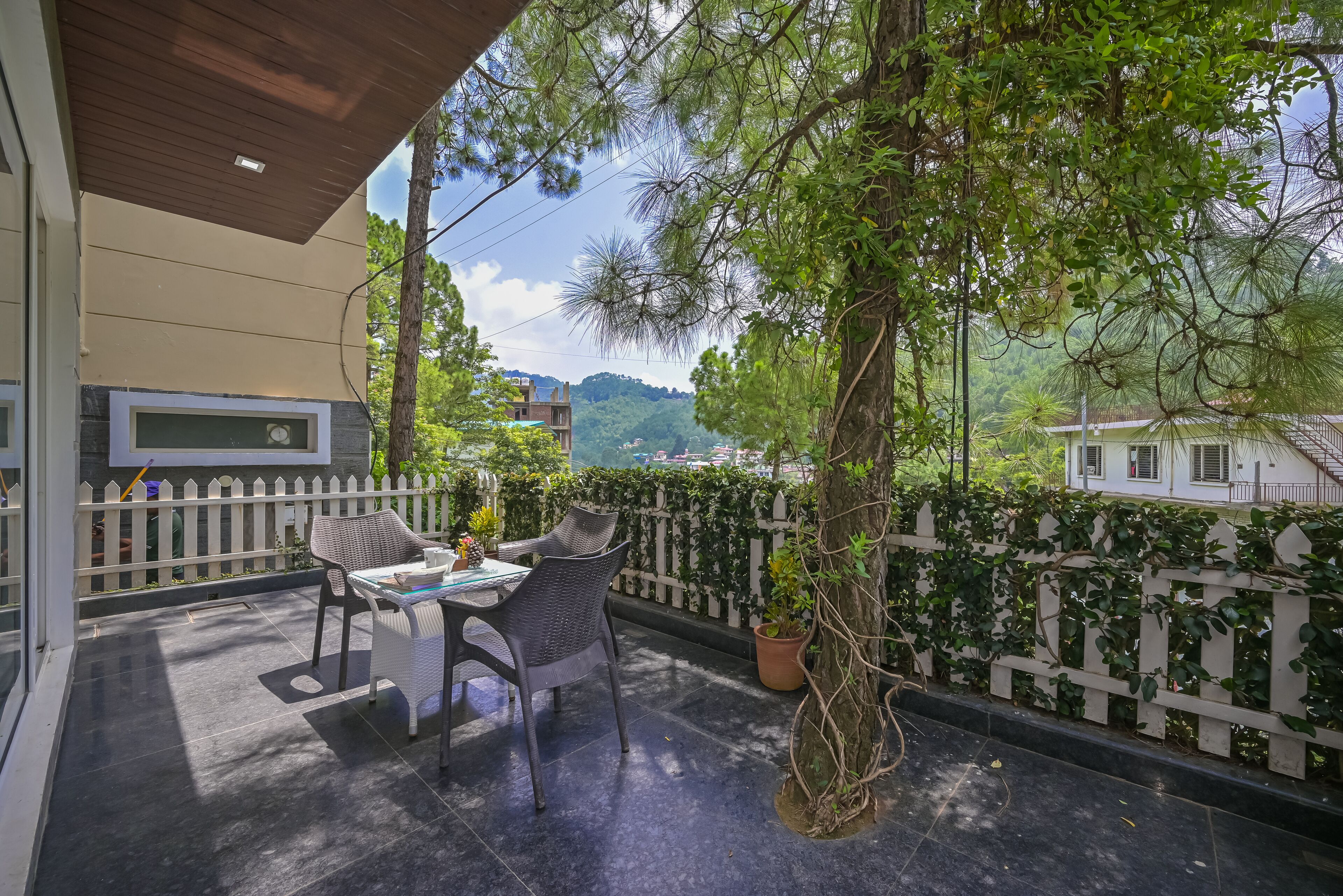 A balcony with a table and chairs, surrounded by a white picket fence and lush greenery.
