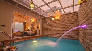 Una piscina interior con cascada, techo de cristal y pared de ladrillo.