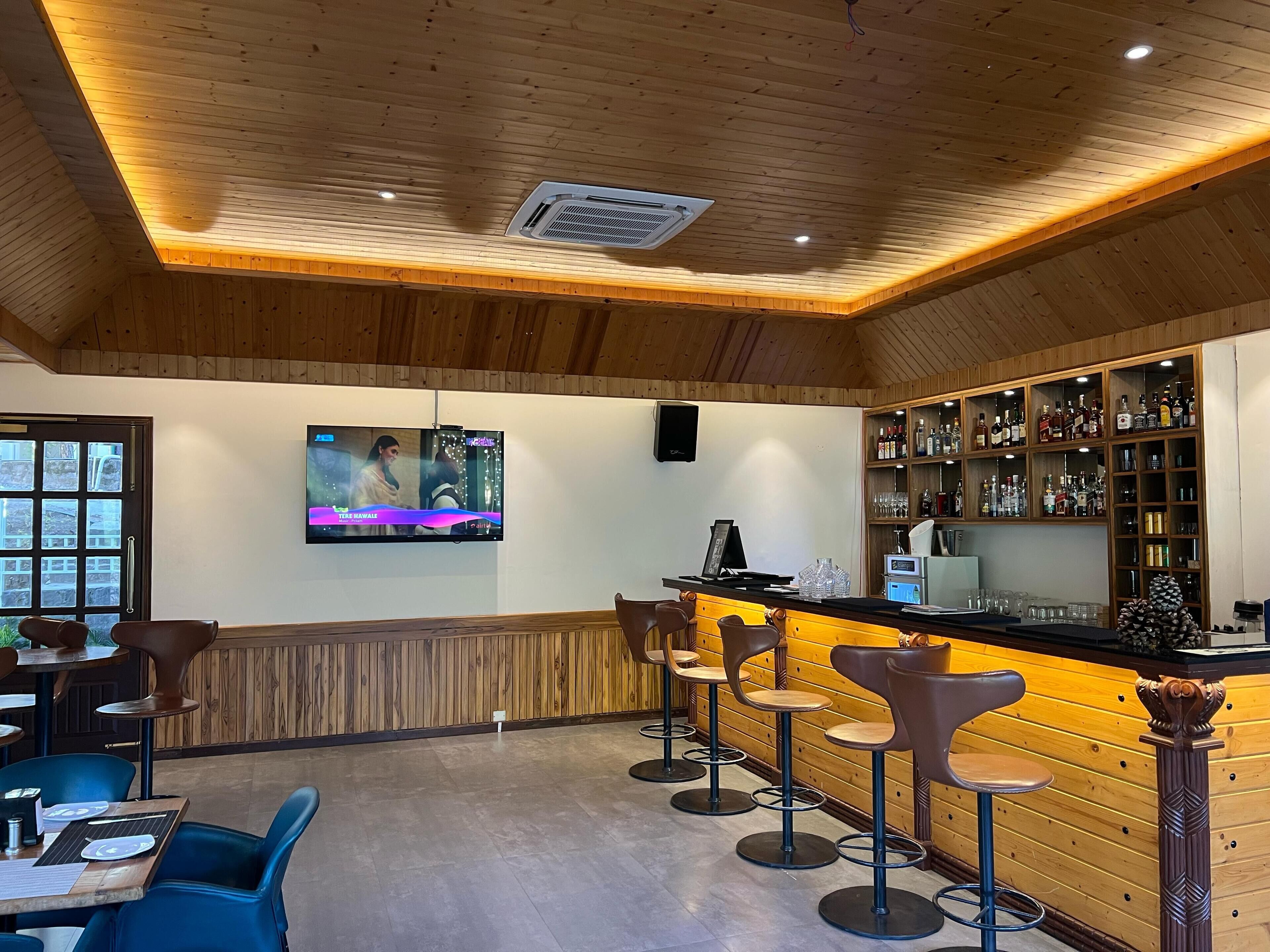 A bar area with wooden paneling, a television screen, and a bar counter with stools.
