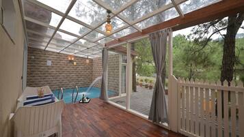 A covered outdoor area with a wooden deck, a pool, and a white fence.
