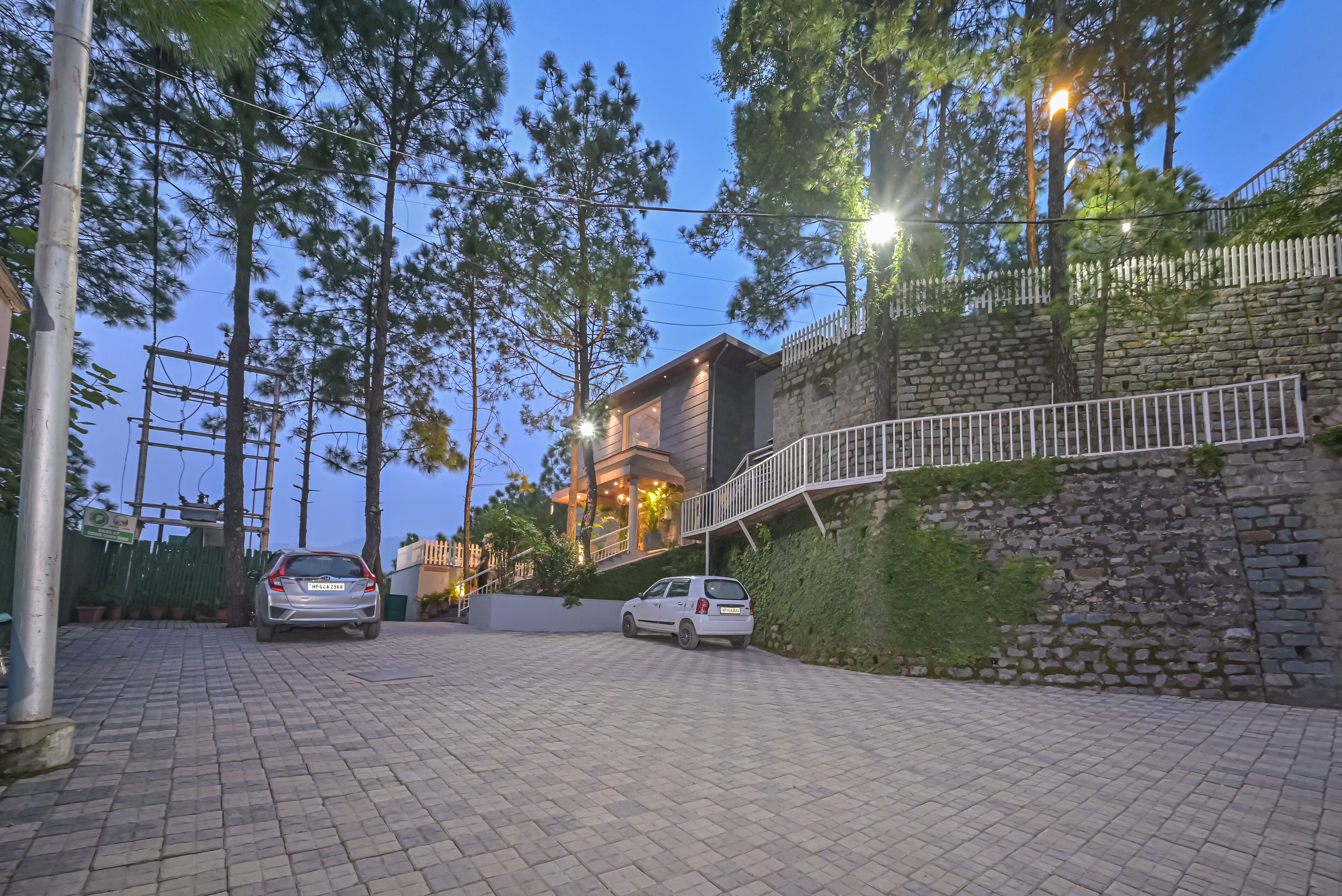 A paved driveway leading to a building with a stone wall and a white fence.