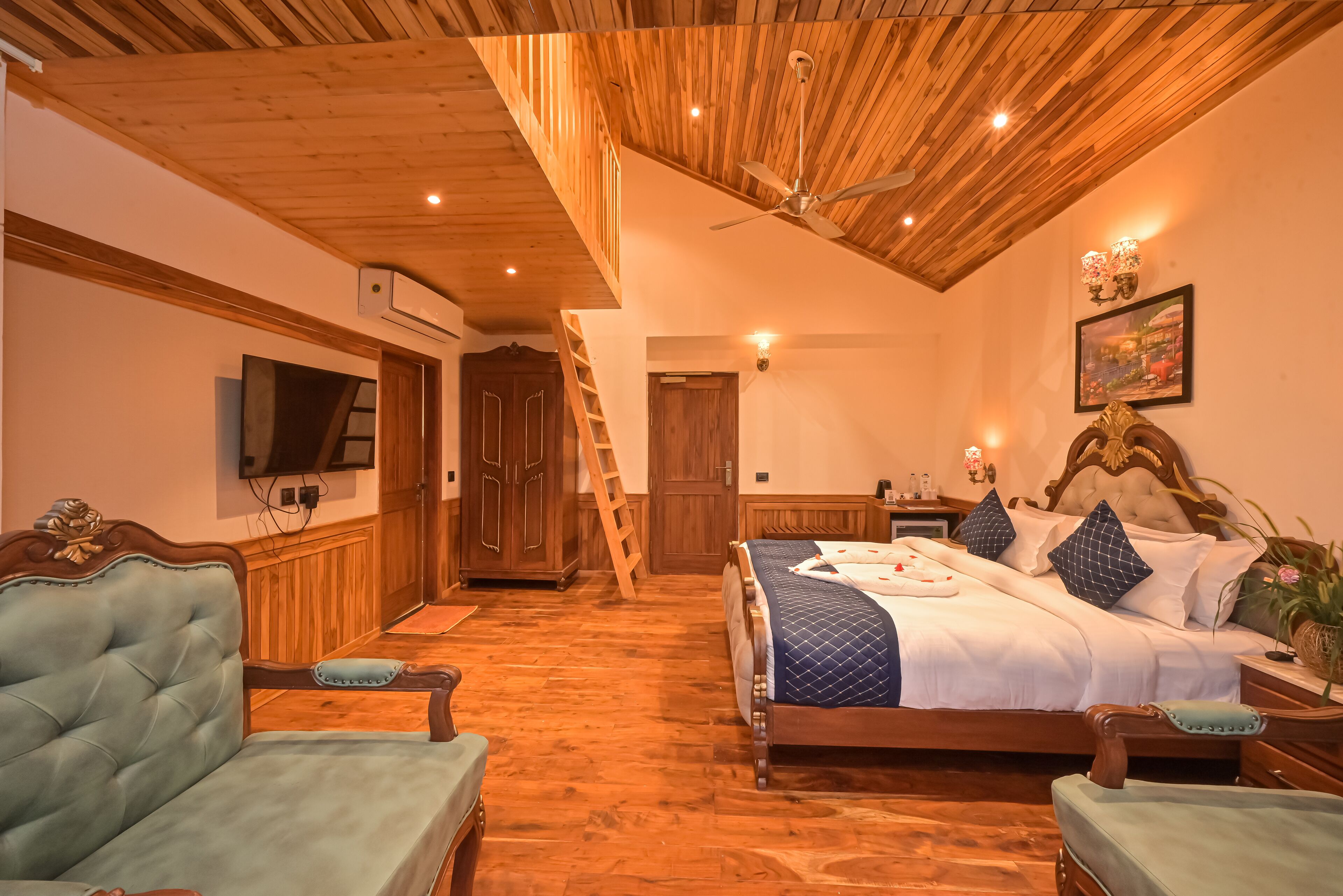 A bedroom with a wooden ceiling, a bed with a quilted cover, a television on the wall, and a wooden wardrobe.
