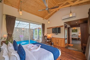 Camera d'albergo con un letto grande, un ventilatore a soffitto, una TV e vista su una piscina esterna.
