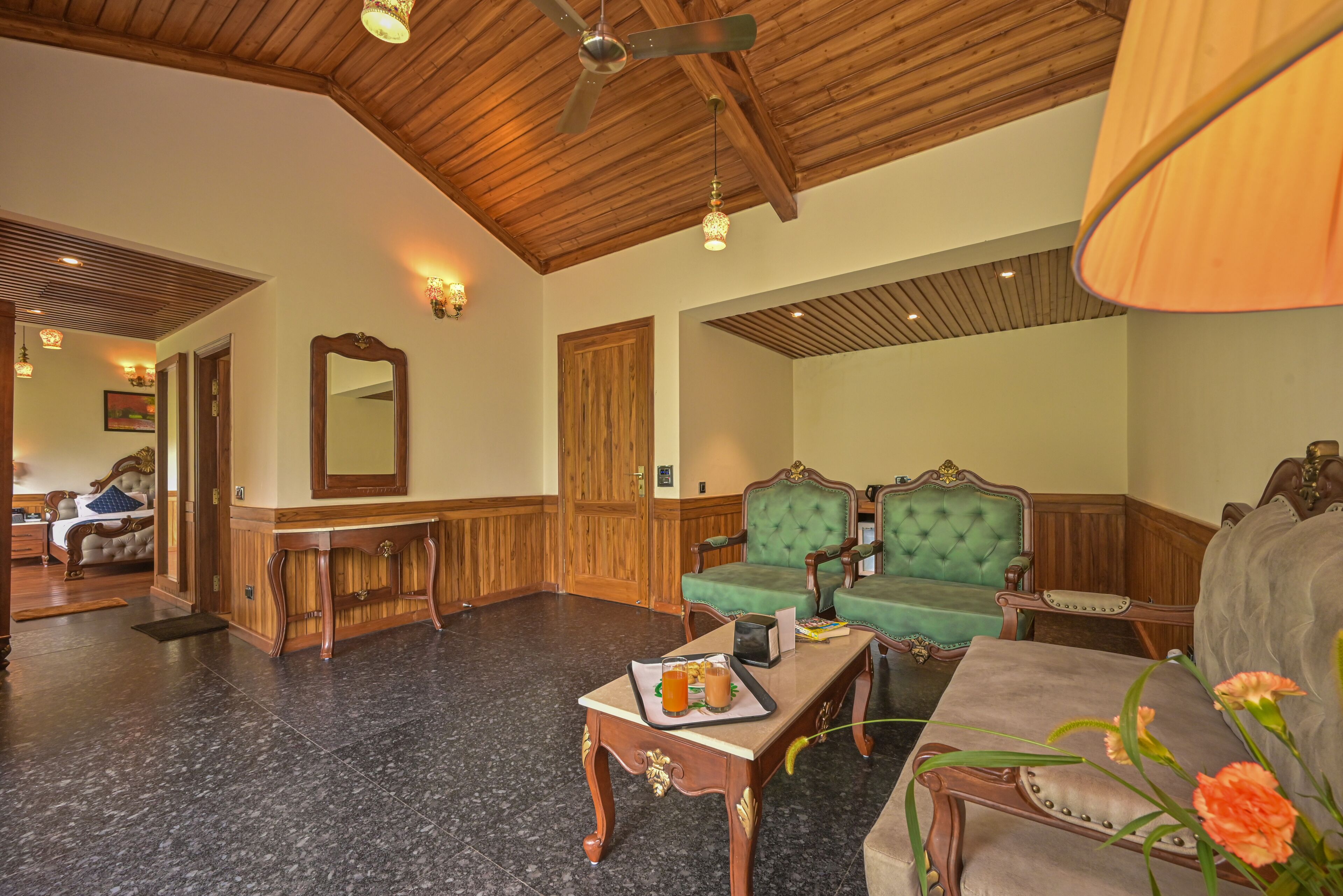 A spacious lobby with a high ceiling, wooden paneling, a grand mirror, and a seating area with green upholstered chairs.