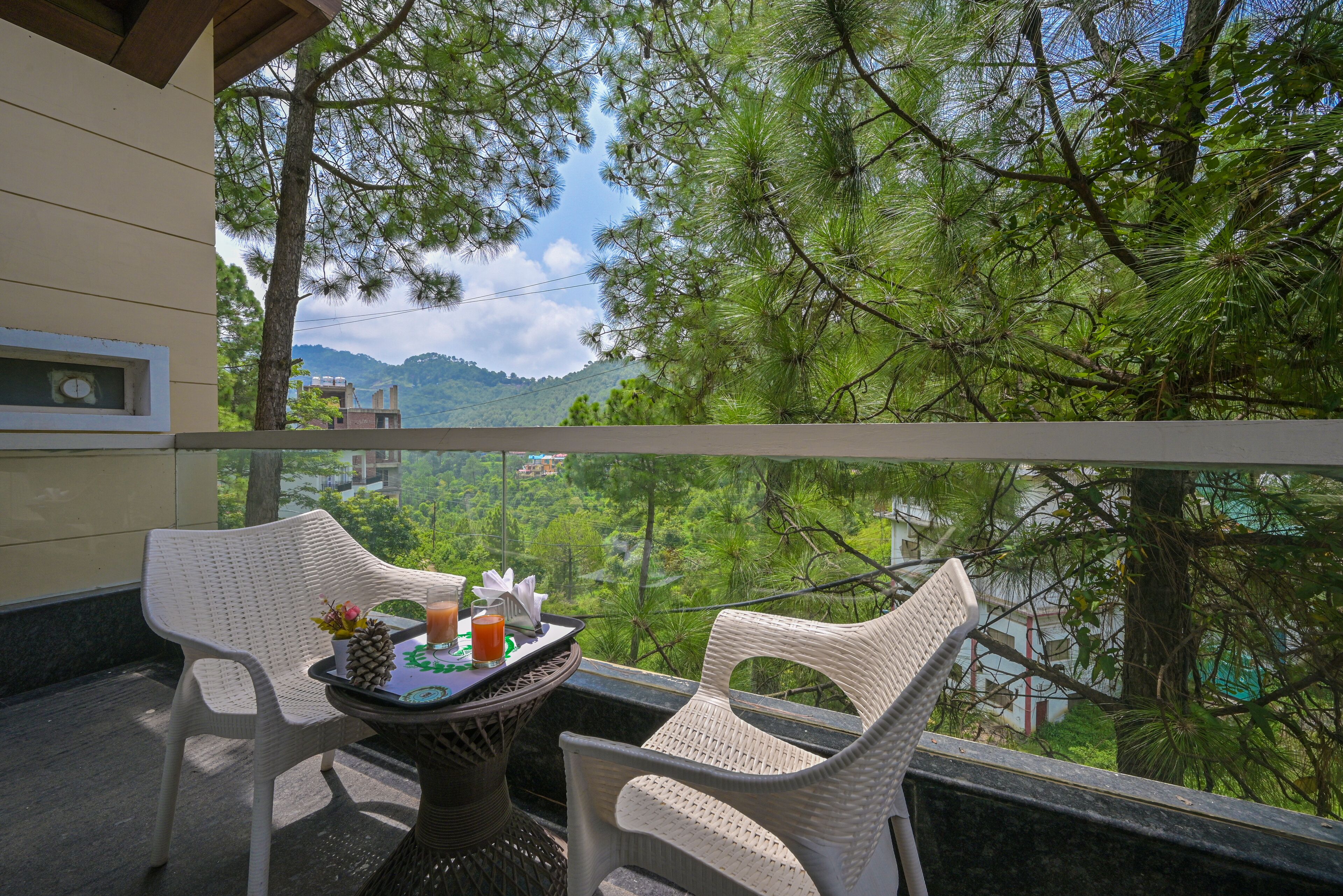 Un balcón con sillas de mimbre y una mesa, con vista a un paisaje verde exuberante y una cordillera distante.