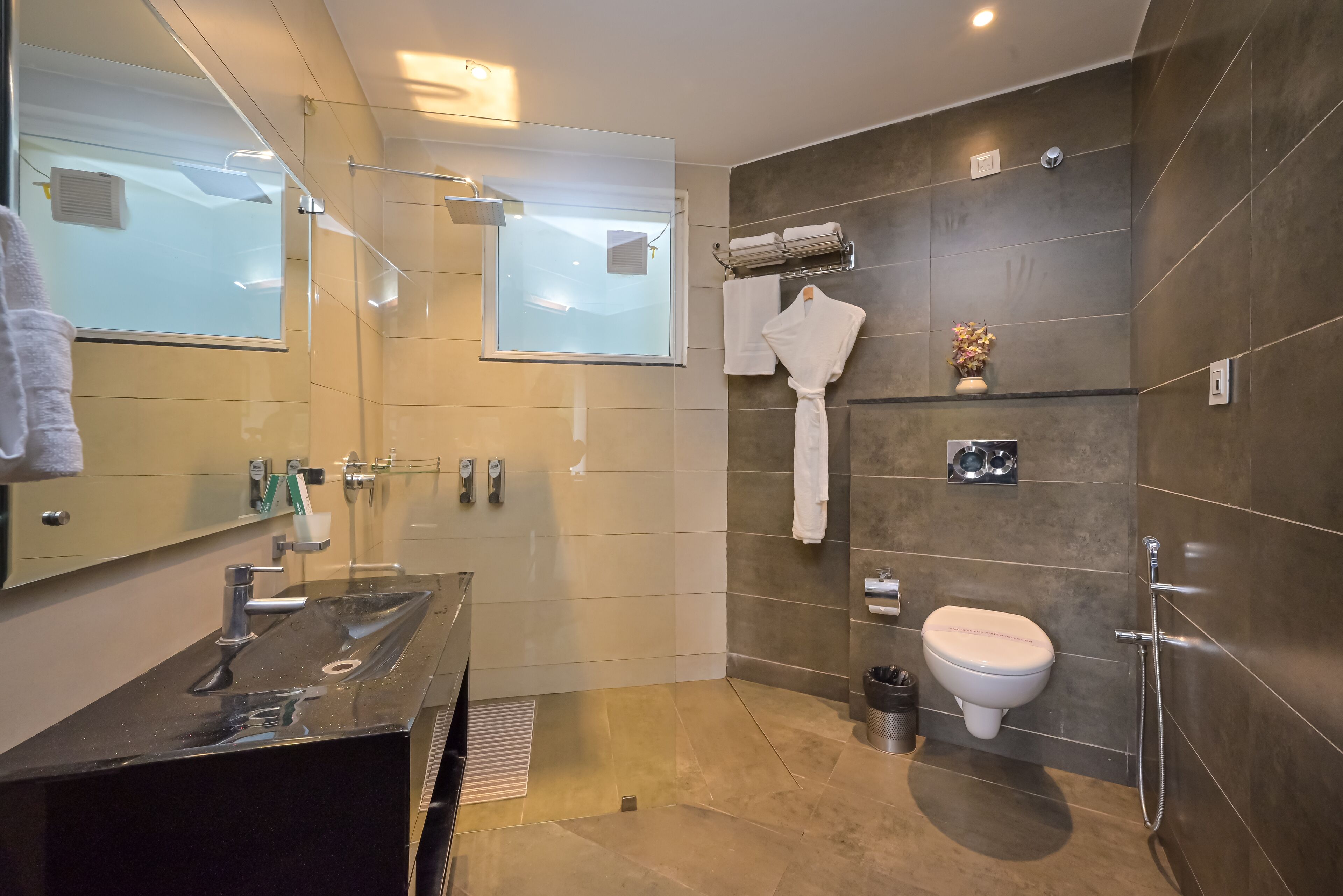 Une salle de bain moderne avec une douche à parois de verre, un meuble-lavabo doté d’un plan de travail noir, des toilettes et un porte-serviettes avec des serviettes.