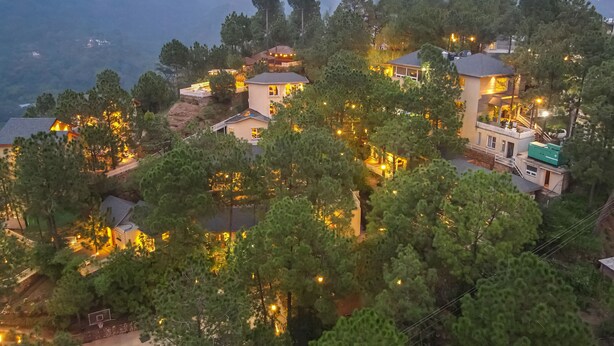 Una zona residencial en una ladera con varias casas, algunas con balcones y escaleras visibles, rodeada de abundante vegetación.